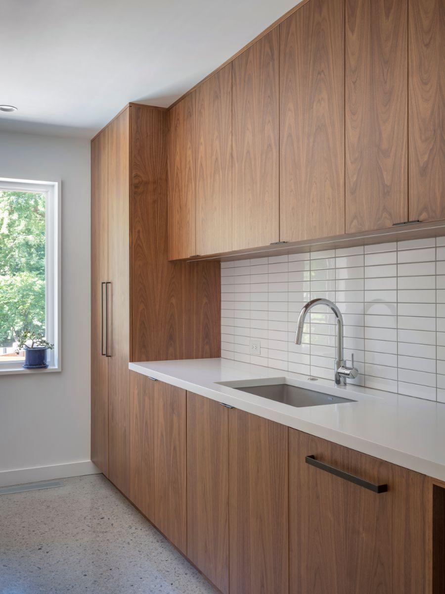 This kitchen features minimalist components such as wood cabinetry, a tile-topped sink, and a wrought iron faucet, as well as views of the garden through the huge window.