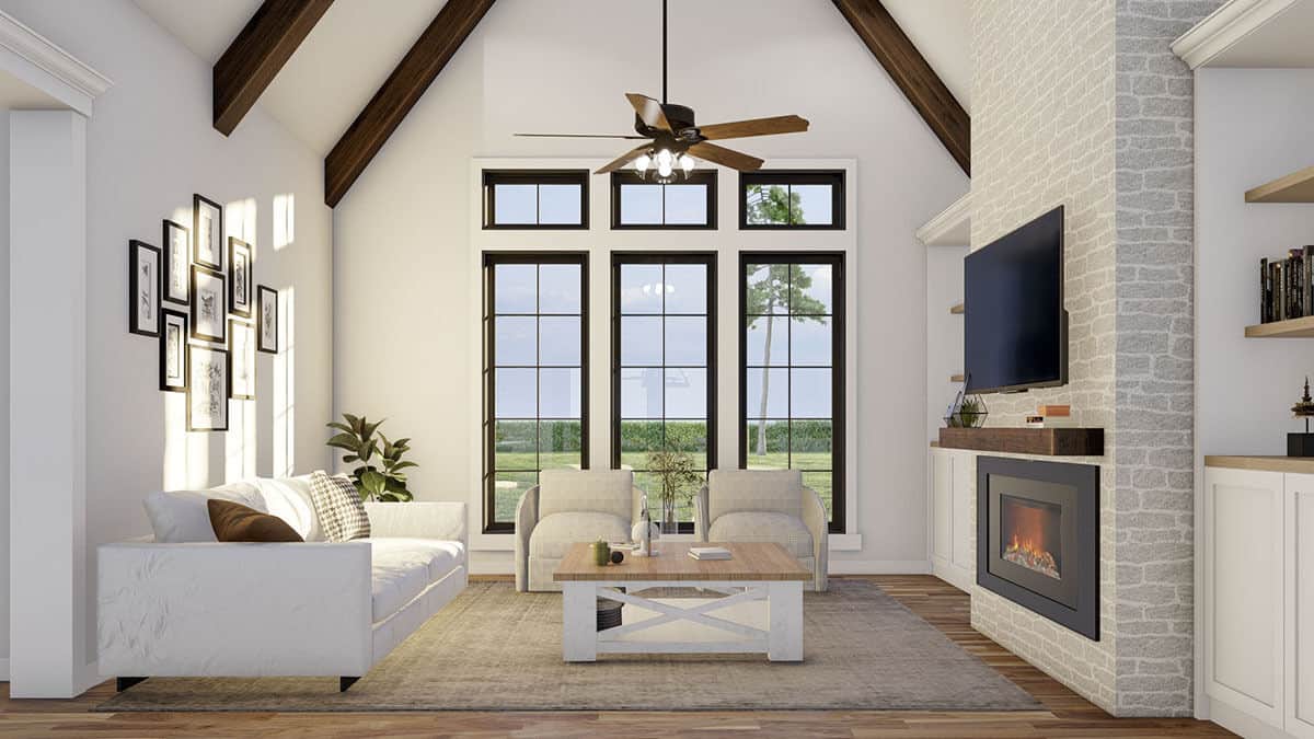 Great room with tall windows, a stone fireplace with a TV on top, and a cathedral ceiling accentuated with exposed wood beams.