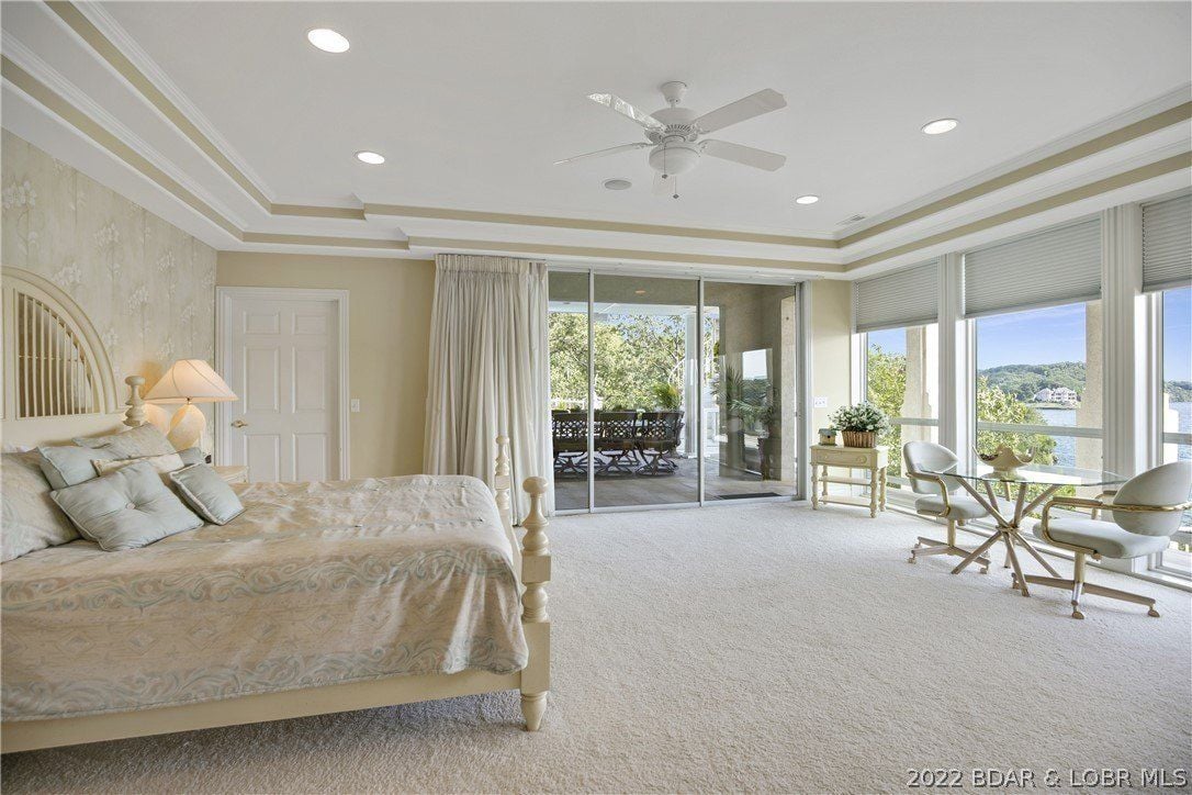 The bedroom features a canopy bed, a wall-to-wall carpet, and glass walls that showcase the view of the lake.