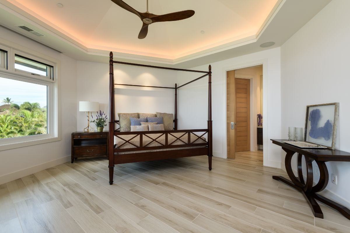 The en-suite room features a four-poster bed and a wooden lampstand table that blends well with wood flooring.