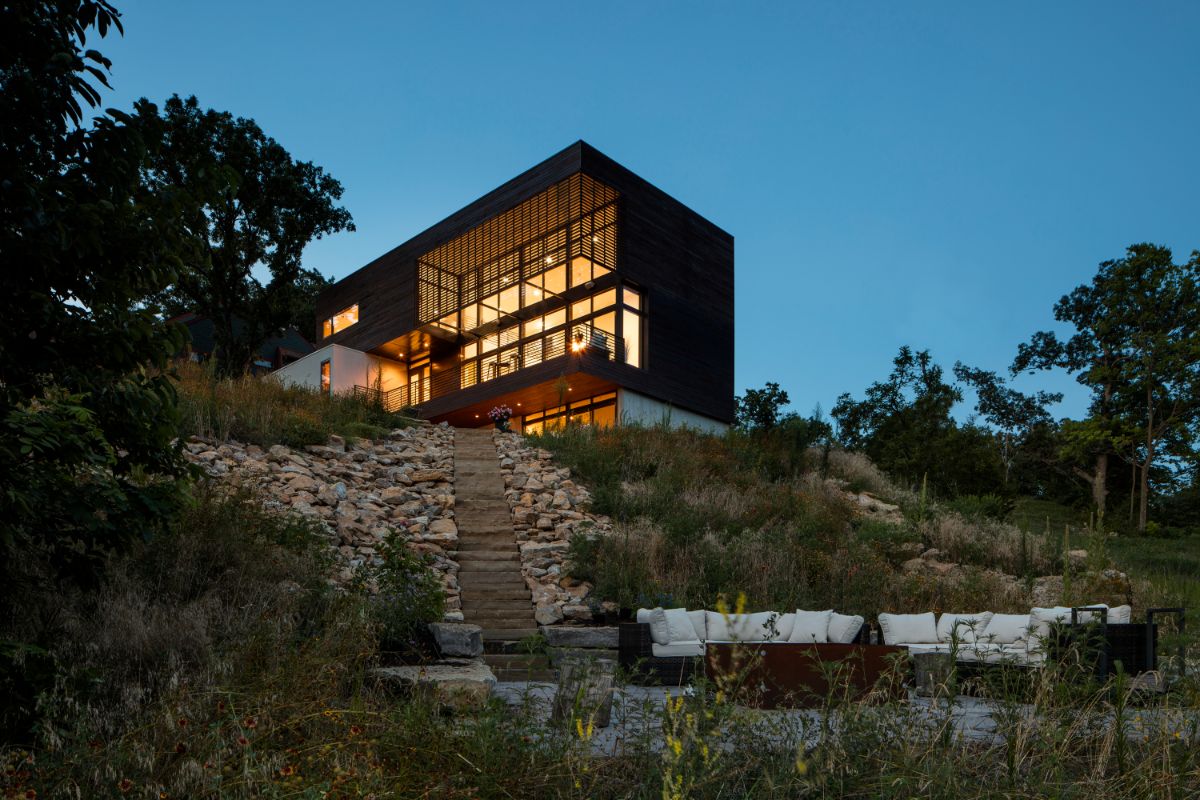 A view of the wood-clad volume with steps leading down to the patio below, ideal for nighttime gatherings.