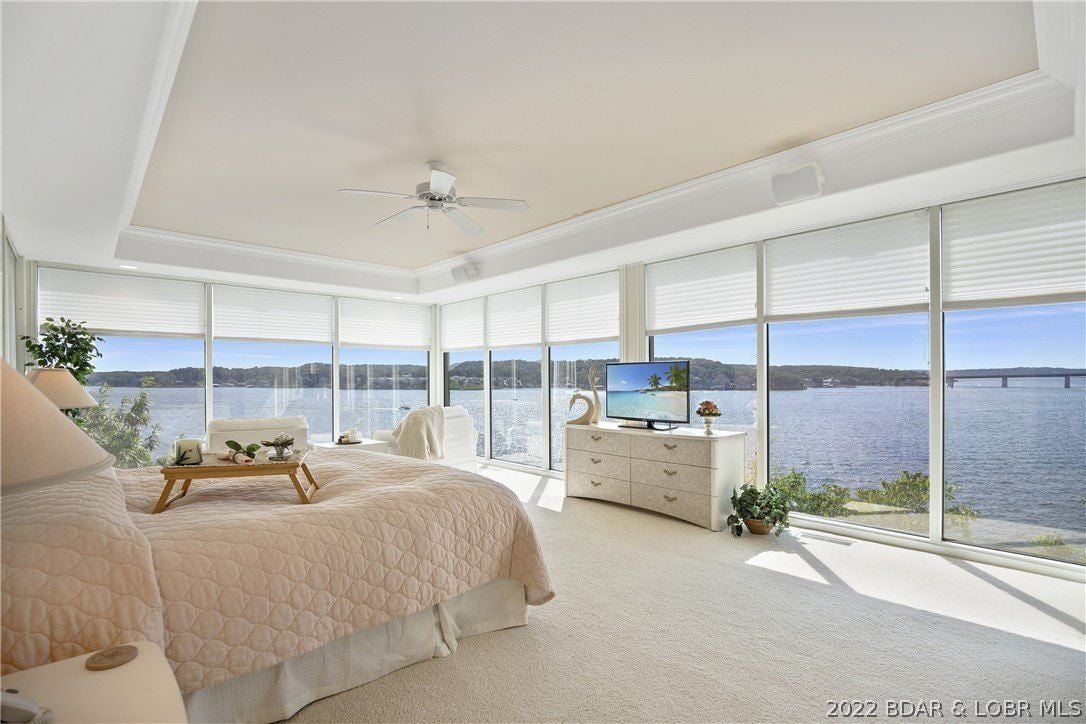 The bedroom features a queen-size bed, and the glass walls showcase the panoramic view of the lake.
