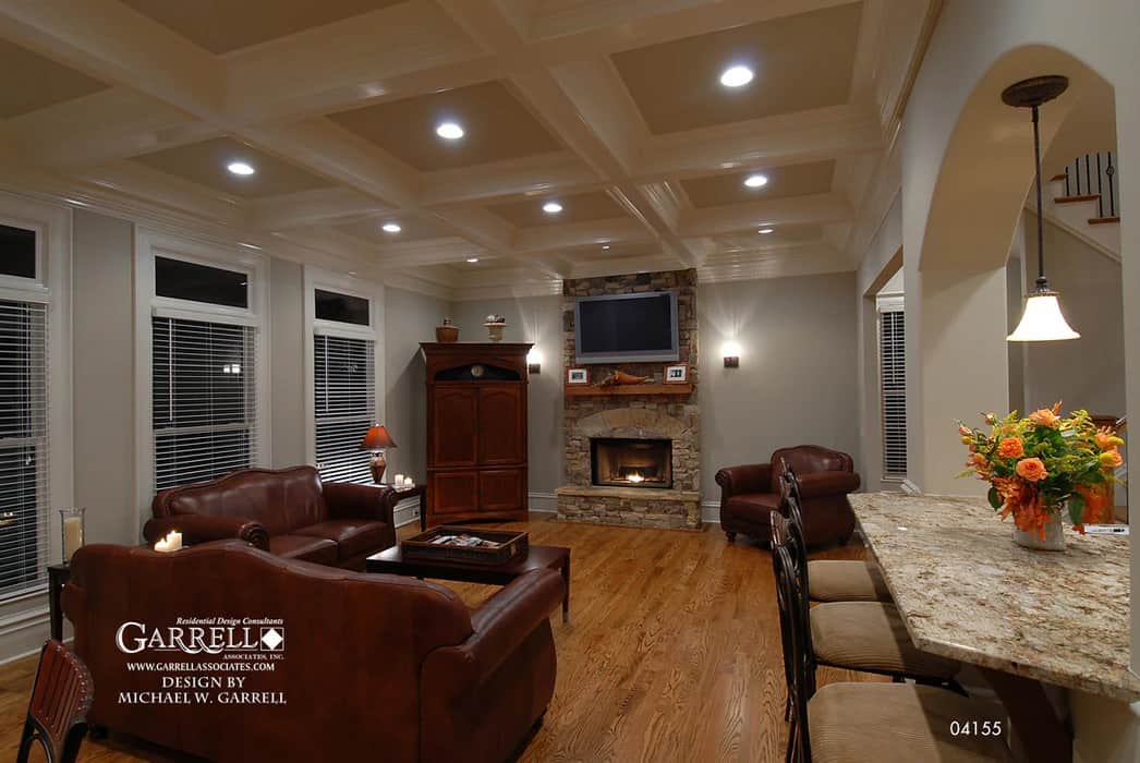 The family room has leather seats, a coffered ceiling, and a stone fireplace topped with a TV.