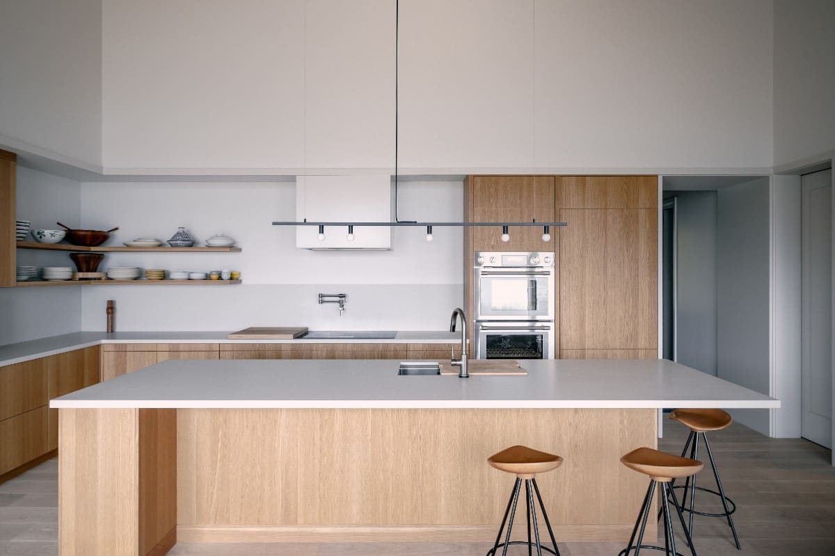 The kitchen offers custom cabinetry, a built-in cooktop, double wall ovens, and a large island topped with a linear chandelier.