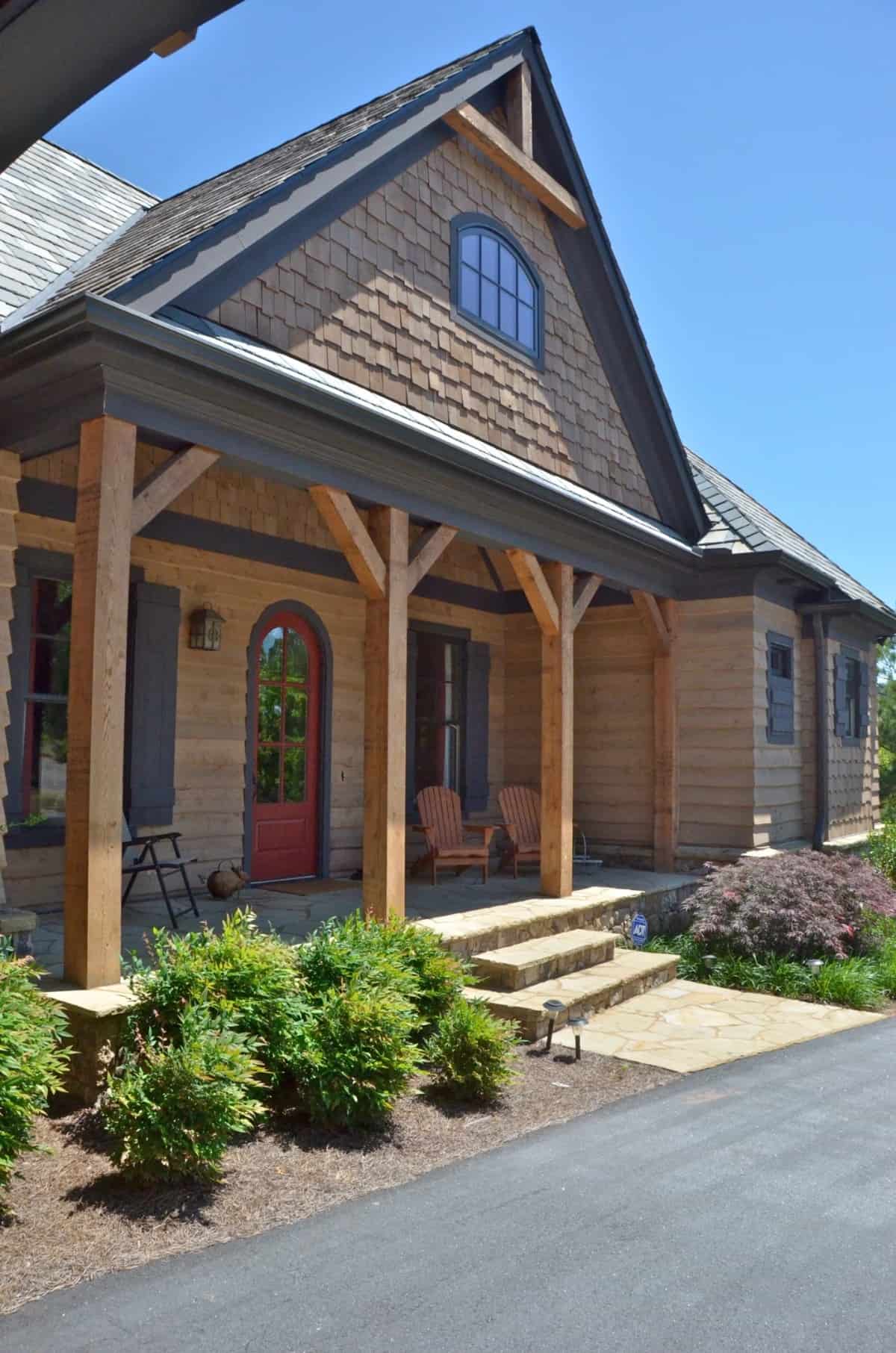 Covered entry porch with a concrete stoop, timber posts, and an arched front door.