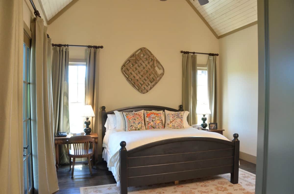 The primary bedroom has a cathedral ceiling and a dark wood bed that blends in with the hardwood floor.
