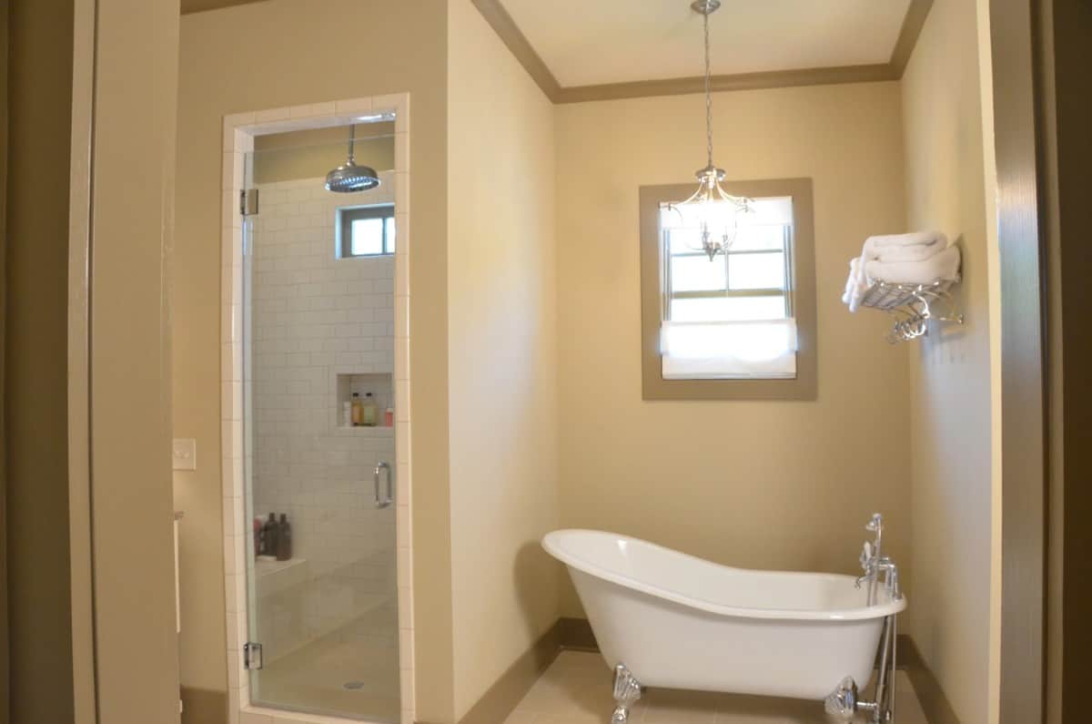 Primary bathroom with a walk-in shower and a clawfoot tub brightened by a framed window and a chrome chandelier.