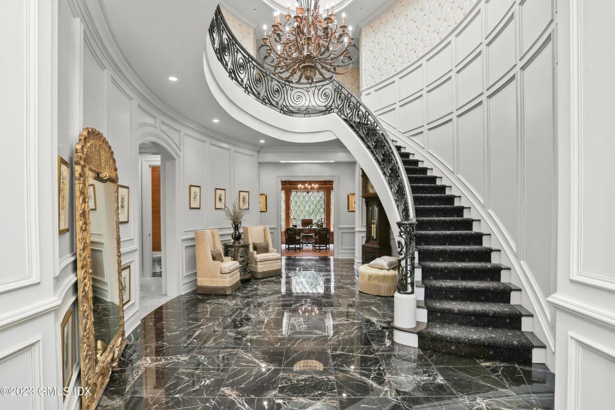 The grand staircase was a breathtaking sight to behold, with its sweeping curves and ornate details, accentuated by the dazzling chandelier overhead that cast a warm, inviting glow across the entire area, creating an ambiance of opulence and grandeur.