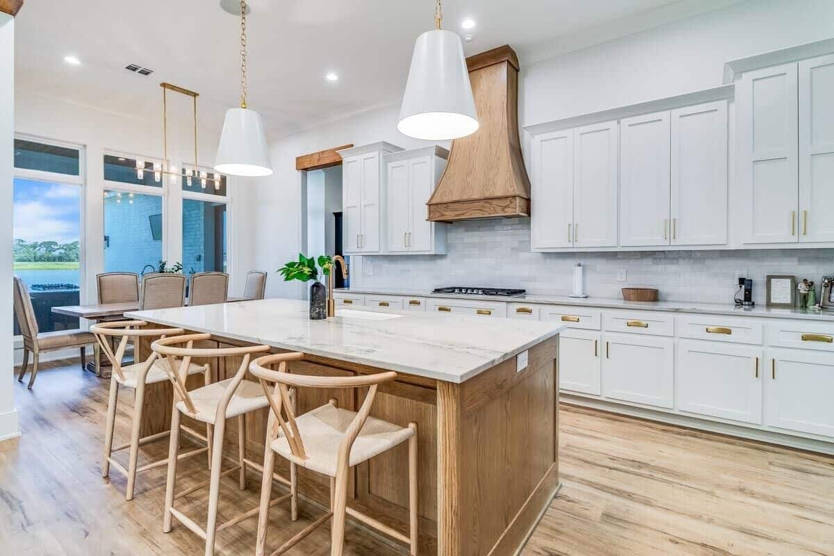 The eat-in kitchen has white cabinetry, a breakfast island, and tall windows that look out the outdoor kitchen.