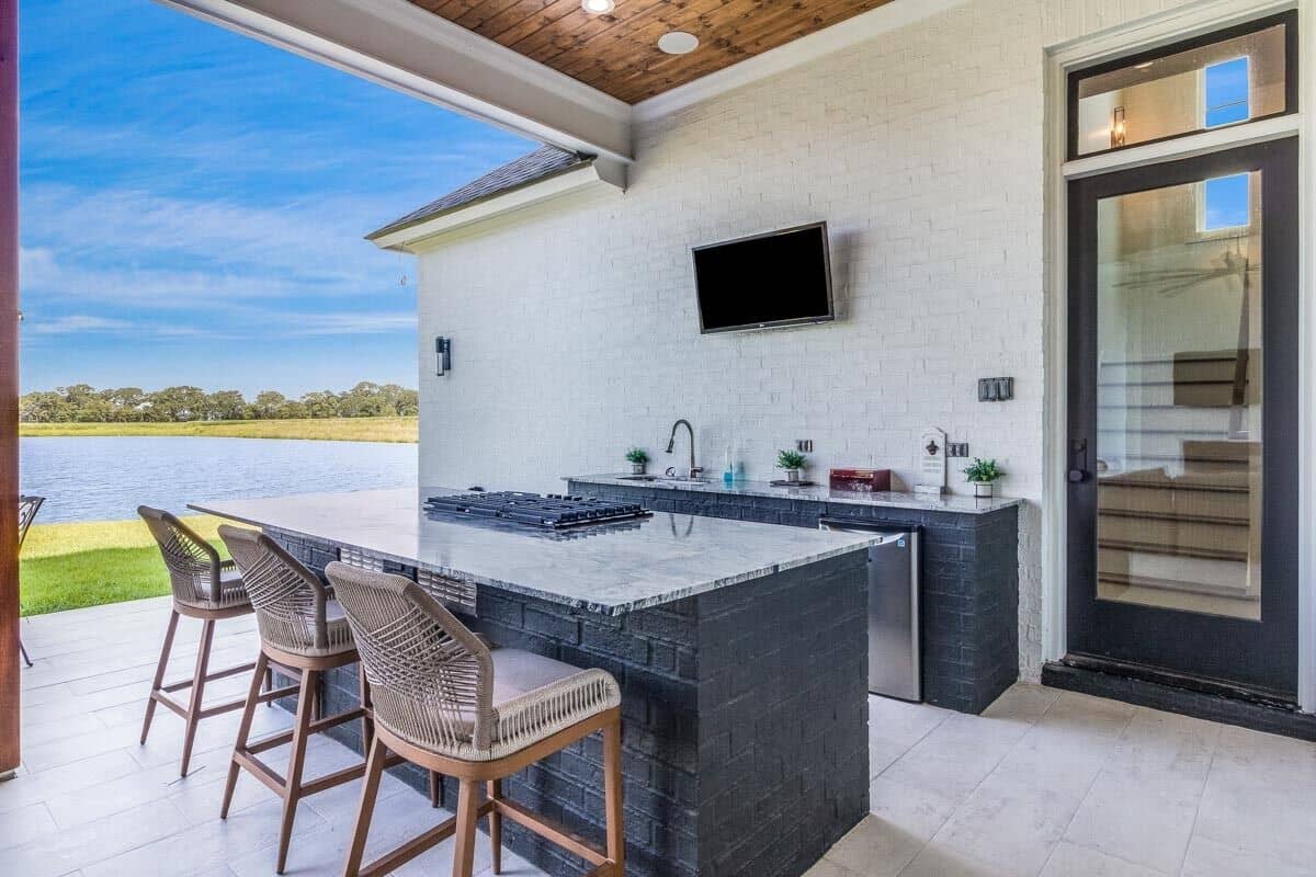 The outdoor kitchen is equipped with undermount sink and a cooktop island paired with wooden bar stools.