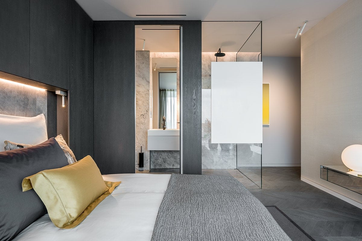A bedroom with warm or grey tones and direct access to a glass-enclosed bathroom.