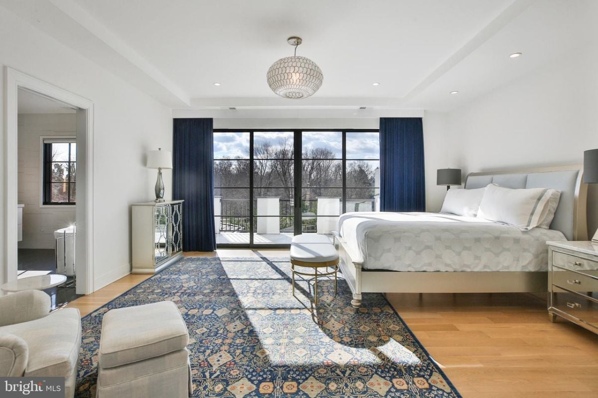In the luxurious primary suite, a stylish bedroom bench sat at the foot of the bed, providing a convenient and elegant seating option. The space was brightened by the natural light that filtered in through the expansive glass doors, creating an airy and tranquil ambiance.