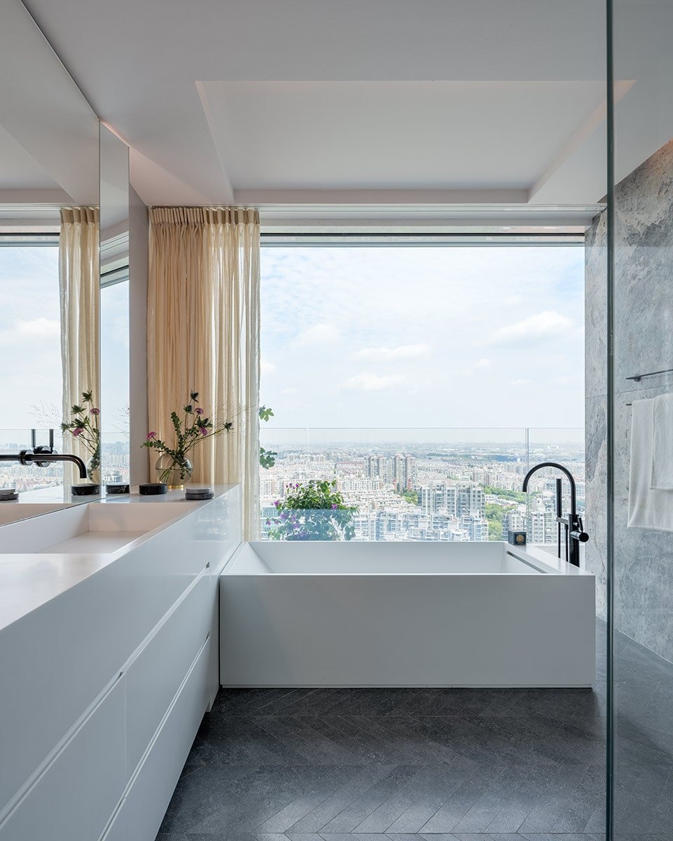 A classic and timeless taste of the bathroom showcasing the white sanitary items and accessories with an overlooking view of the city from the wide window.