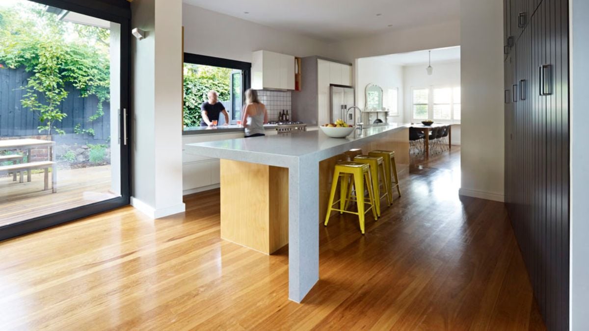 The kitchen contains white island counter made of cement and wooden floors.