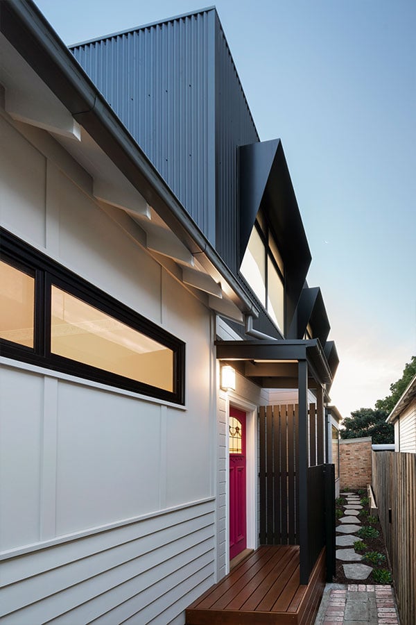 The house's main entrance, with the pink door standing out against the white wall and dark timber cladding.