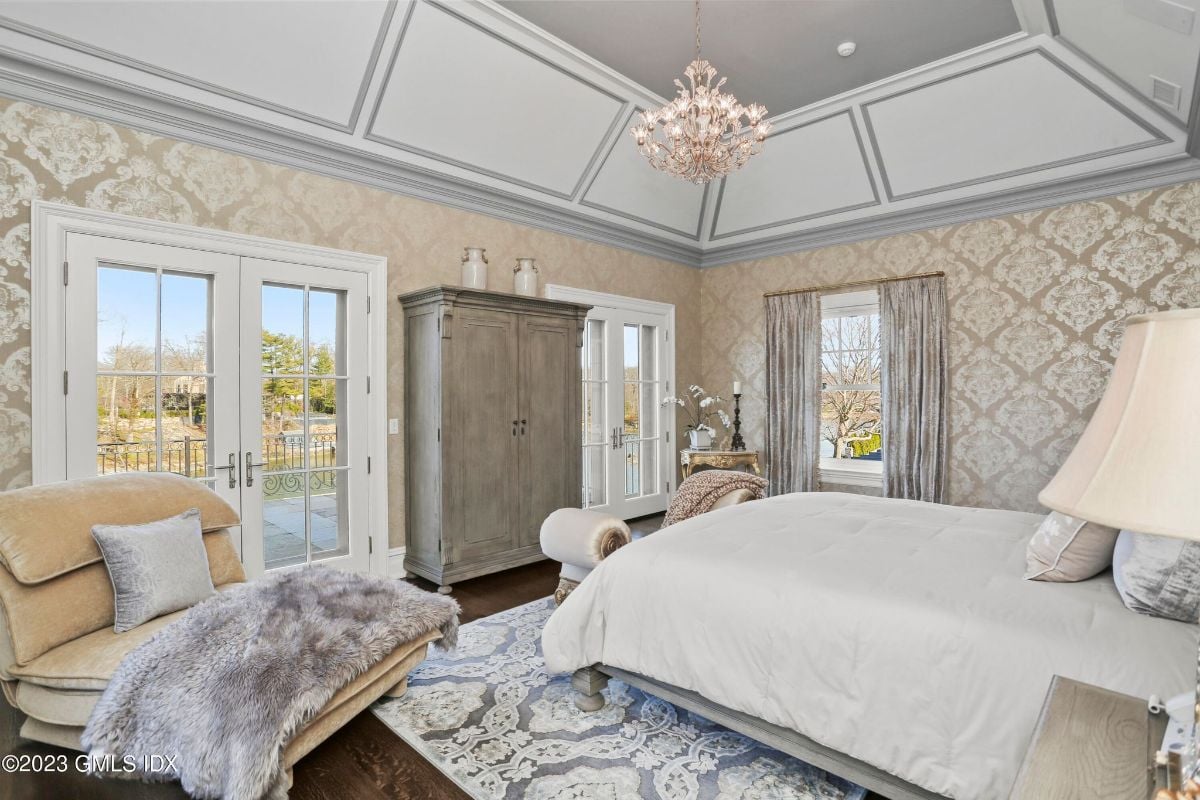 The bedroom was a picture of elegance, with a sumptuous bench placed at the end of the bed, bathed in the soft glow of a resplendent chandelier that added a touch of glamour and sophistication to the space.