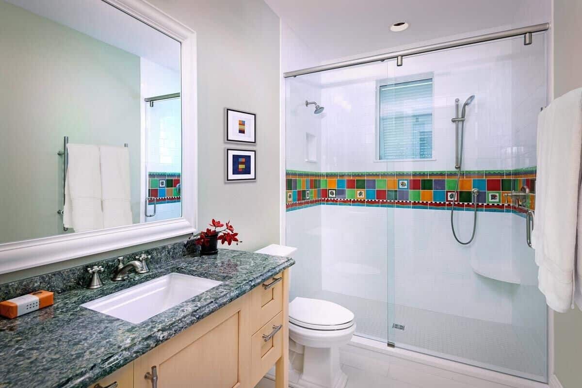 This bathroom is equipped with a sink vanity, a toilet, and a walk-in shower accentuated with colorful mosaic tiles.