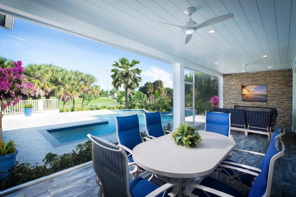 The covered lanai includes an outdoor dining set with an oval table and blue cushioned chairs.