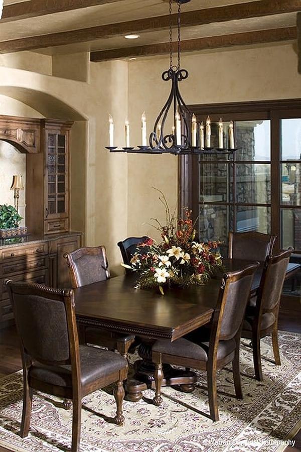 The formal dining room offers a candle chandelier, a classic area rug, leather upholstered chairs, and a wooden dining table topped with decorative flowers.