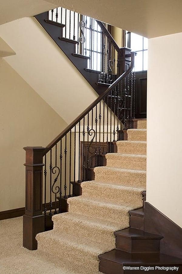 Traditional staircase with ornate railings and dark wood steps covered in a beige carpet.