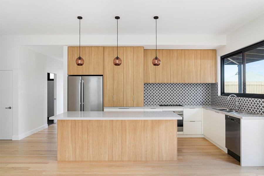 A kitchen with built-in high-end appliances, a patterned backdrop, pendant lighting, and a tile-topped island.