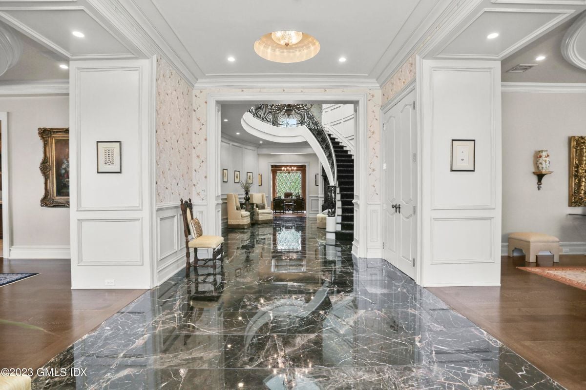 Stepping into the grand foyer of the mansion, I was greeted by a magnificent stair case that ascended towards a mesmerizing chandelier, illuminating the entire area with its dazzling light.