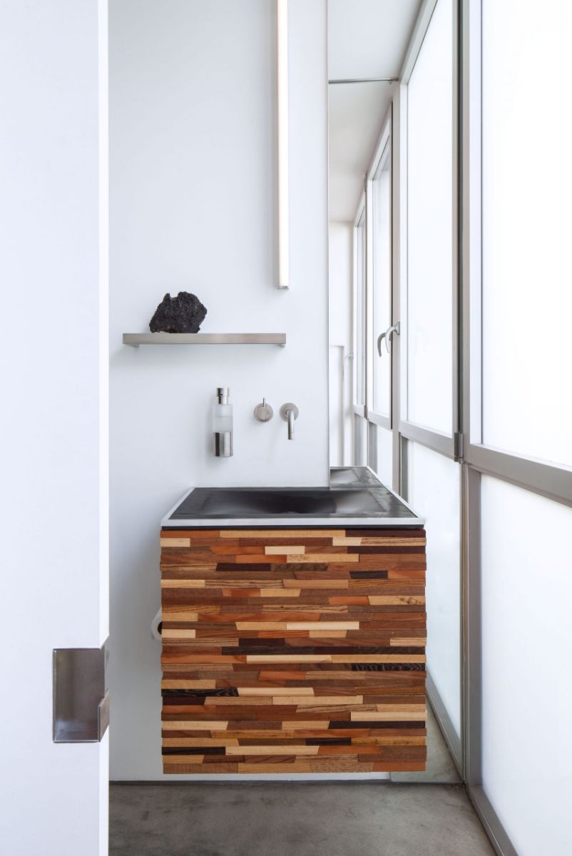 A light-filled bathroom with a sink mounted in floating prefabricated panels with wrought iron fixtures.