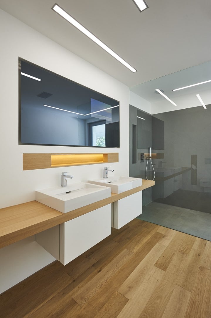 The bathroom, which has a dual sink situated on a floating counter, with a full-width mirror and a walk-in shower.