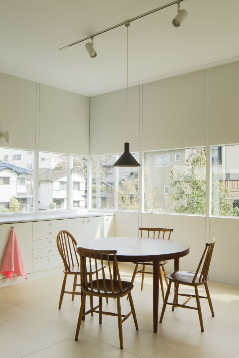 The dining room, which has a four-seater round table, pendant lighting, and a view of the neighboring houses through a glass slit.