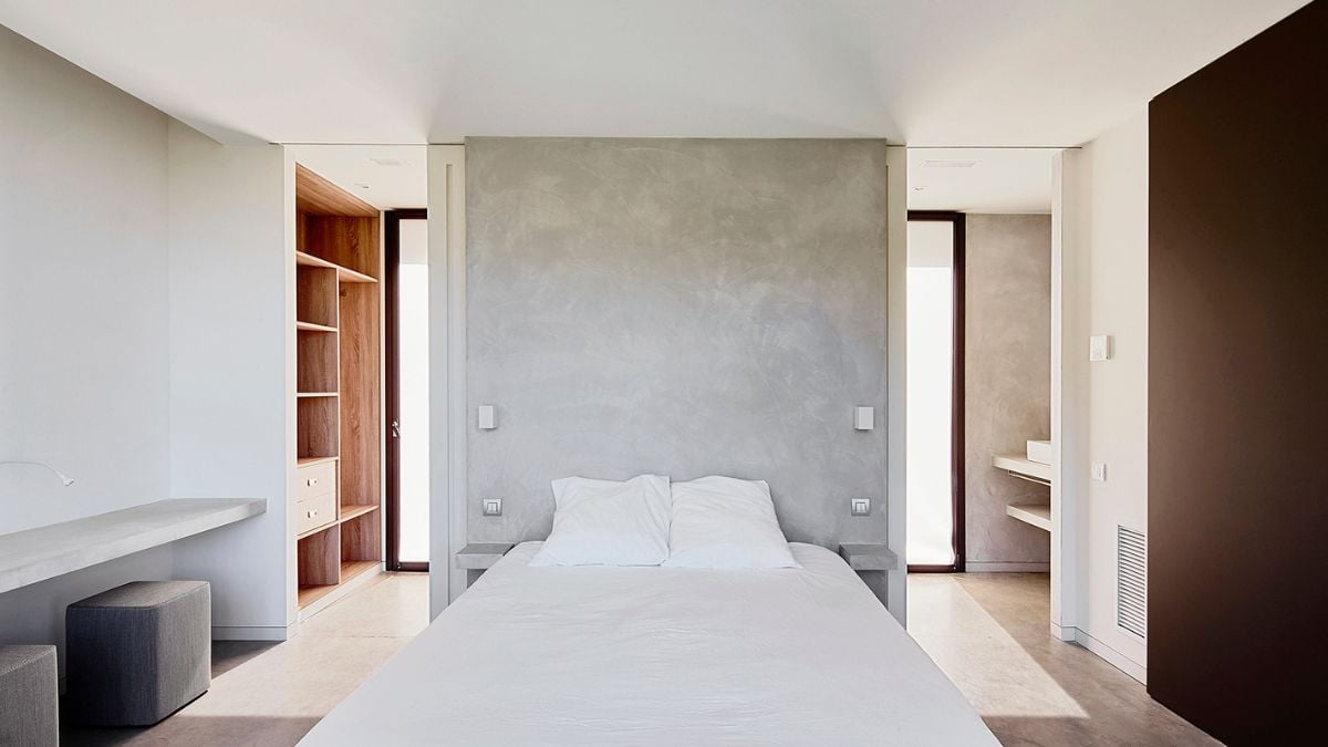 The bedroom has white sheets and bedding, paint that is a mix of white and grey, and wooden cabinets.