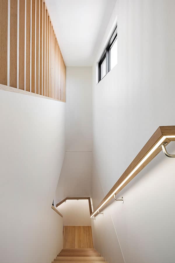 A stairs with wooden steeps and railings, white walls, and a small window that lets in natural light.