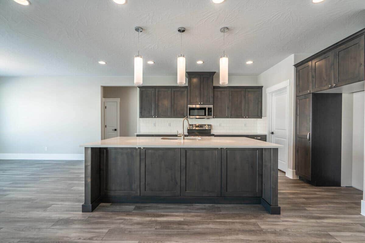 Kitchen with dark wood cabinetry and a breakfast island illuminated by cylindrical pendants.