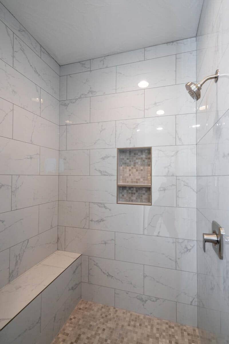 The white marble tiles are echoed in the walk-in shower with chrome fixtures and a tiled bench.