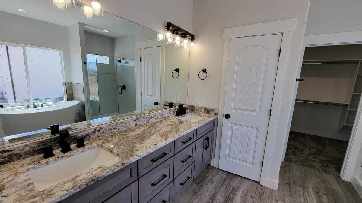 The primary bathroom features a dual sink vanity topped with a large rectangular mirror and warm sconces.