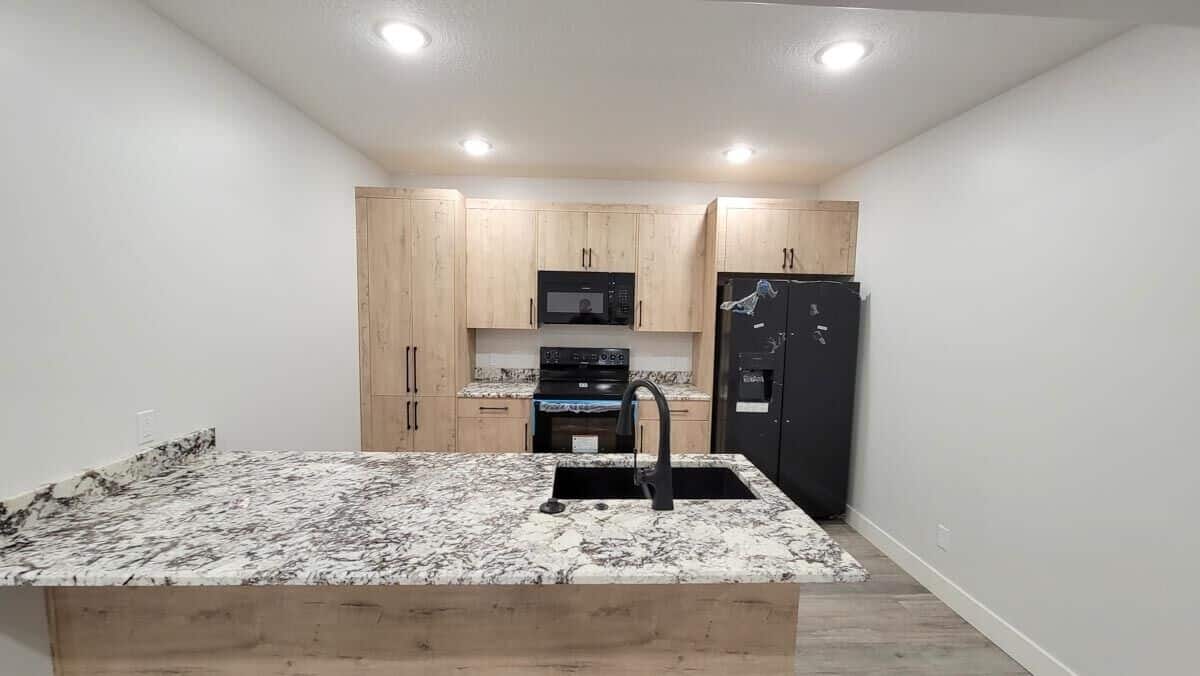 Lower level kitchen with light wood cabinets, black appliances, and a peninsula bar.