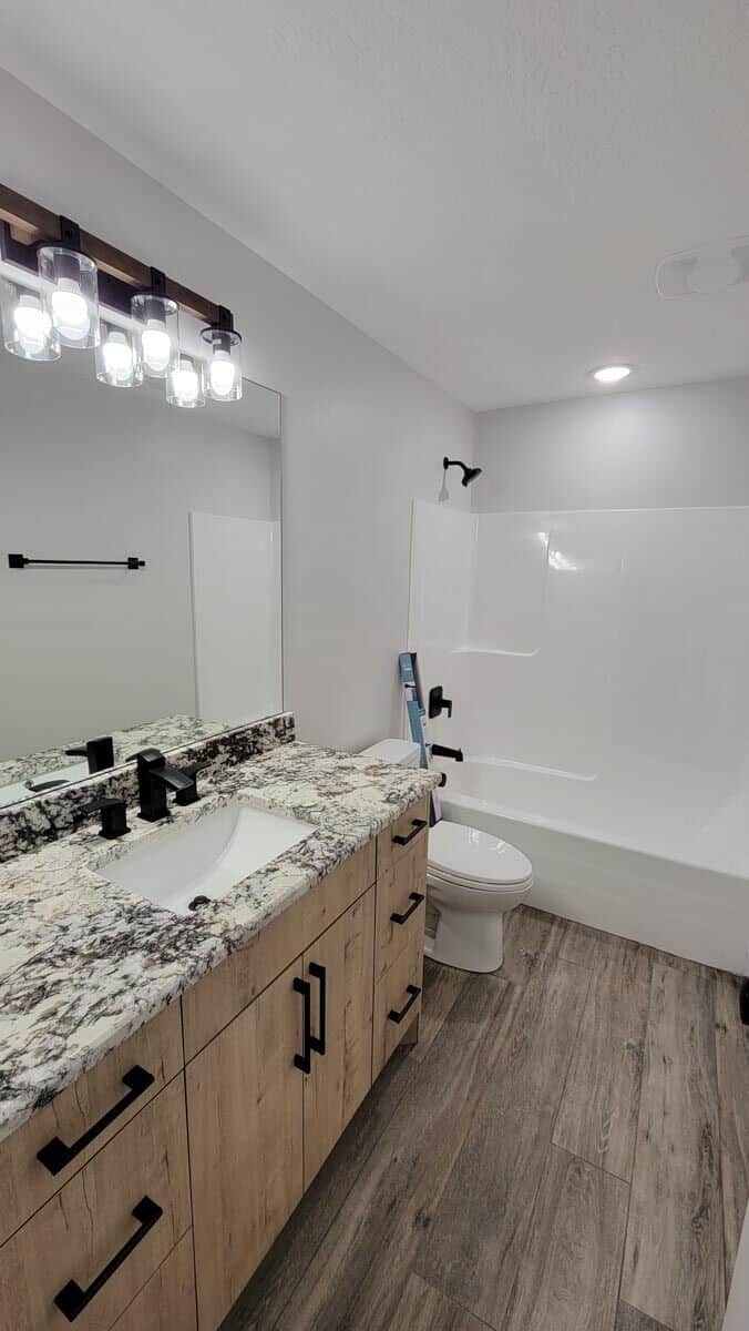 This bathroom has a tub and shower combo and a single sink vanity accentuated with wrought iron fixtures and hardware.
