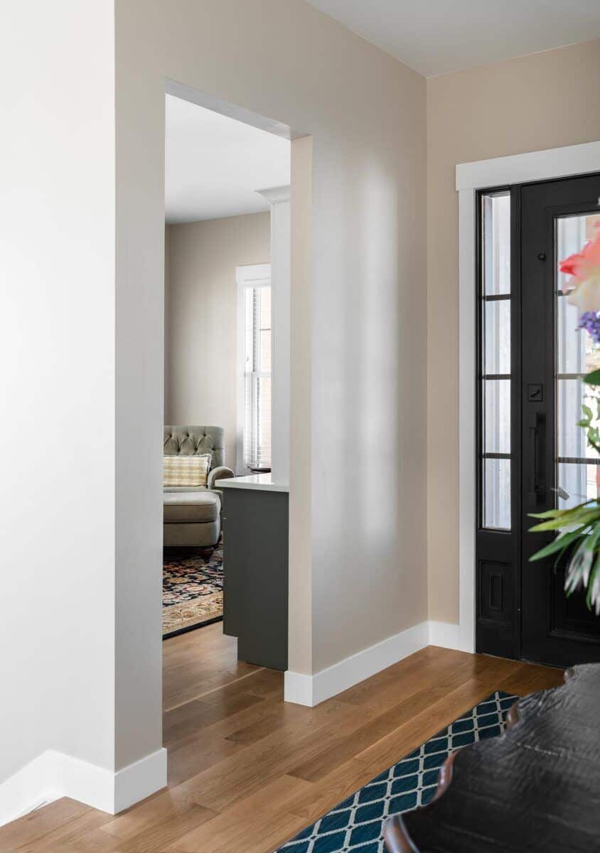 The foyer has a glazed entry door and a patterned rug over the hardwood floor. A door on its side reveals the quiet den.