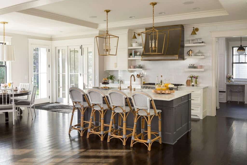Kitchen with white cabinets, matching floating shelves, and a breakfast island topped by oversized brass pendants.