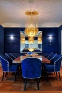 Electric blue cobalt walls and wood inlay floors take center stage in this incredible modern dining room. Bold yellow and orange abstract art hangs on the wall opposite the wood sideboard and drapes that adorn the window.