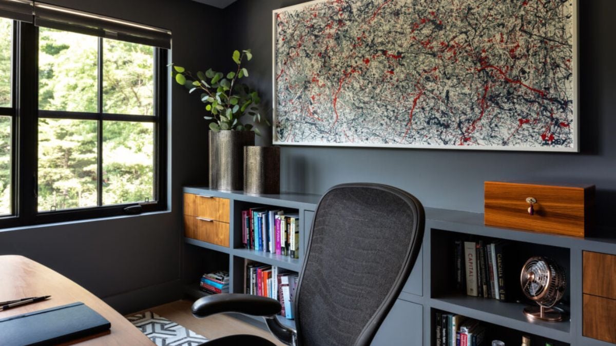 Black walls and bookshelves below the wall-mounted artwork make up the office space.