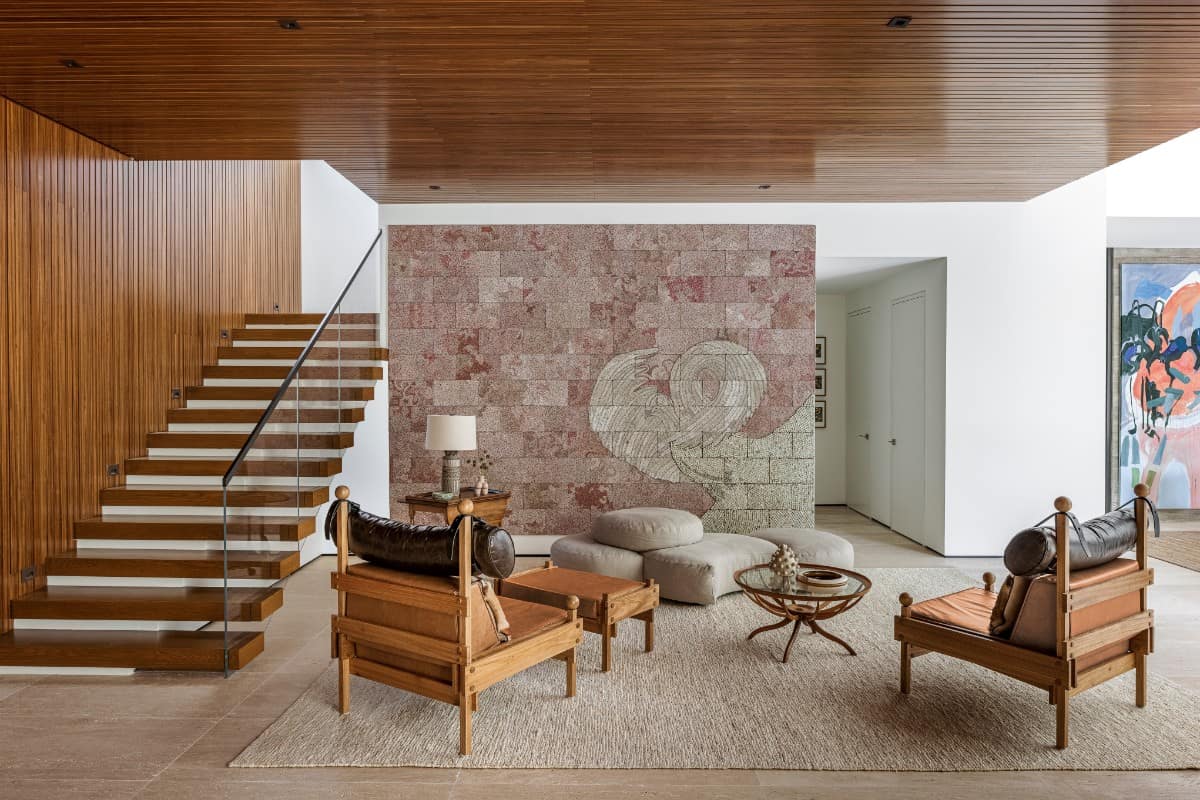 The space between the living and dining rooms feature a Giuseppe Scapinelli coffee table, Sergio Rodrigues armchairs, and Elias Simeโs Tightrope: I Want to Slow Down and Think, 2017.