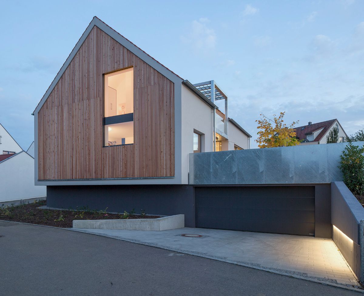 The dwelling-house's front face is a modern, rural structure with a red saddle roof, a natural color scheme, and a material mix of larch wood and hot-dip galvanized steel.