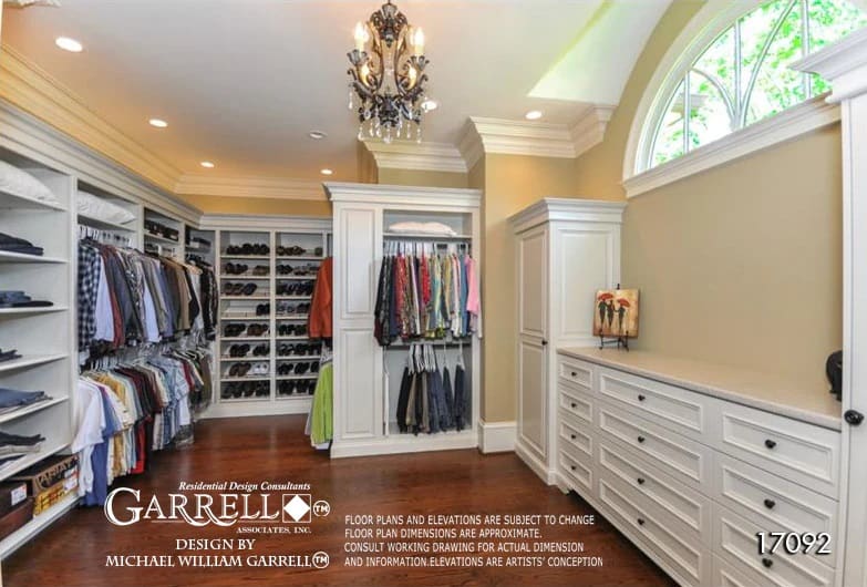 Spacious walk-in closet illuminated by warm recessed ceiling lights, wrought iron chandelier, and an arched transom.