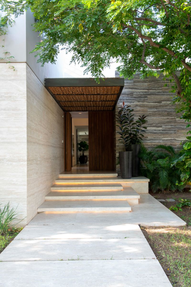 The house's main entry, with a concrete walkway leading to a wooden double door. The plants and trees helped to create a welcome ambiance.