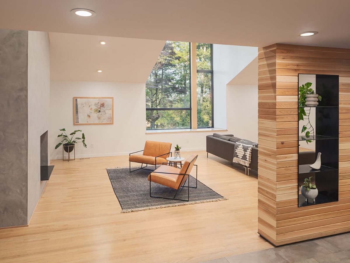 A bright living room with lightwood flooring, a fireplace, recessed lighting, and a view of the outdoors through the wide cedar dormer.