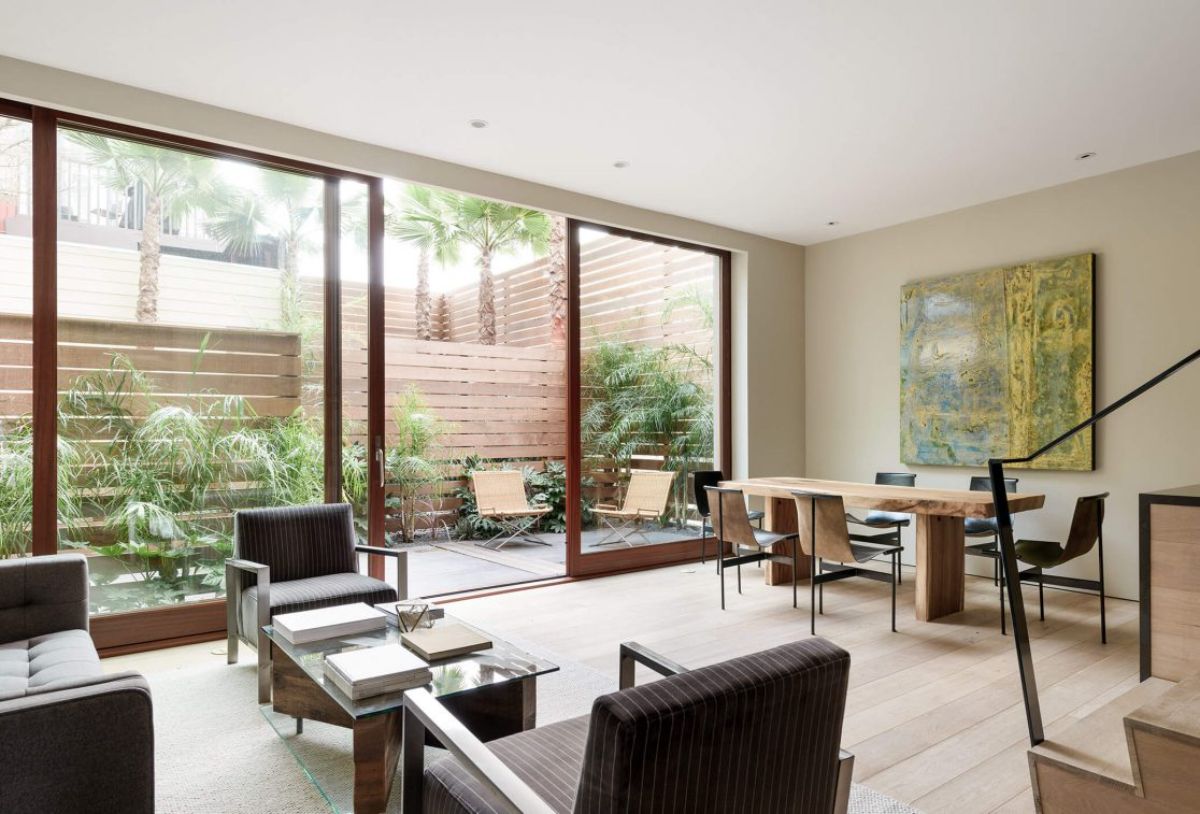 A light-filled open layout of living, dining, and kitchen in "garden house" unit. The fixtures are made of natural wood, glass and steel. The large sliding floor-to-ceiling door leads to a garden area.