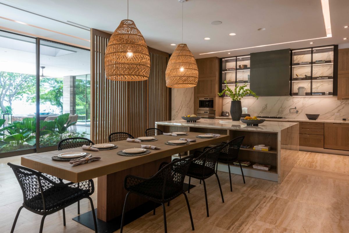The dining space, which includes a wood dining table and woven chairs. It is adjacent to the kitchen and features a marble-topped island. Pendant and recessed lighting illuminated the space.