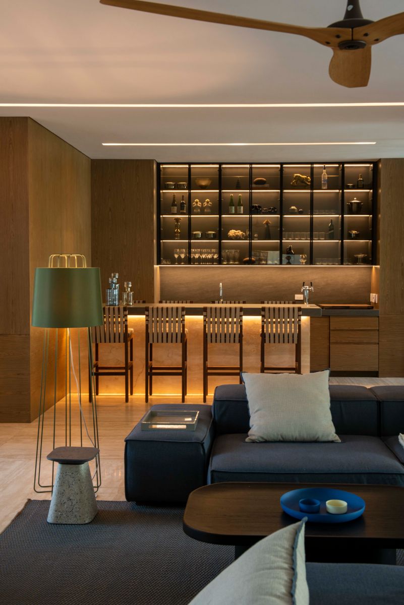 The bar area, which has a bar counter and wall-mounted clear storage. It has a rug in the seating area, and the blue sofa and dark brown wooden table compliment one other.