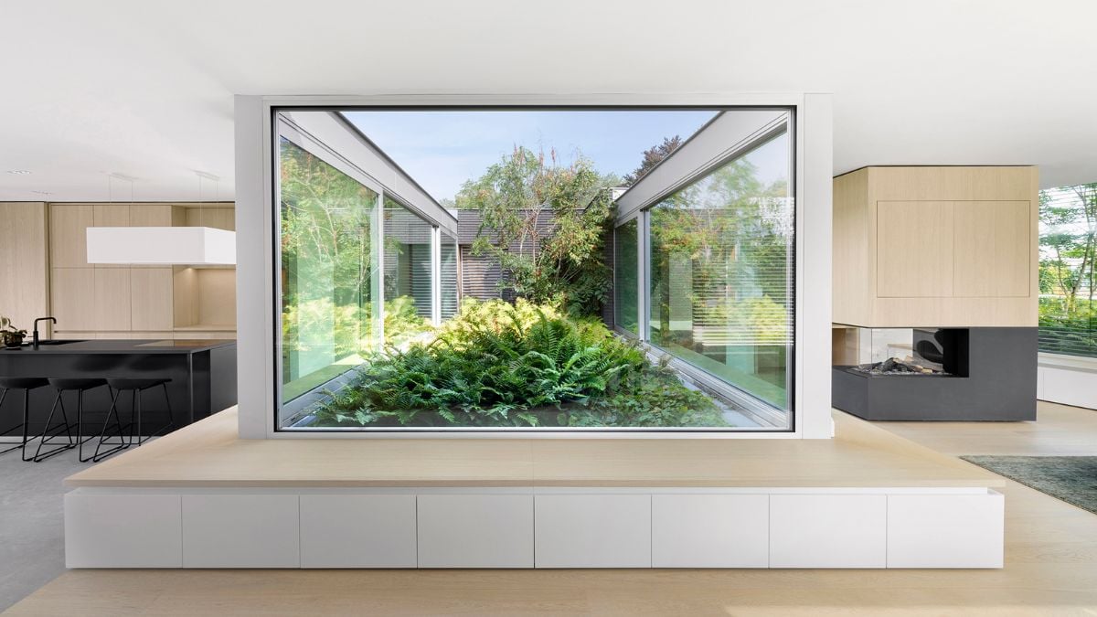 A lush green patio is situated in the middle of the living space, and floor to ceiling sliding doors provide unobstructed views of the backyard garden and swimming pool.