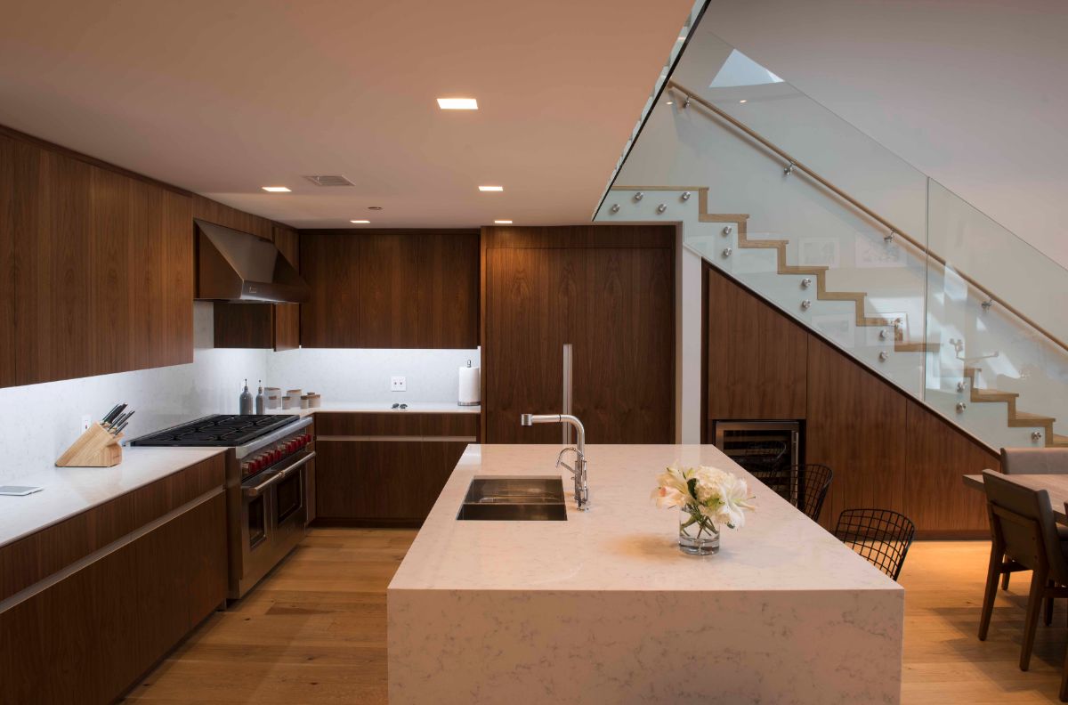 A minimalist kitchen with a marble island and built-in equipment, as well as a white kitchen counter that contrasts with the dark brown counter.